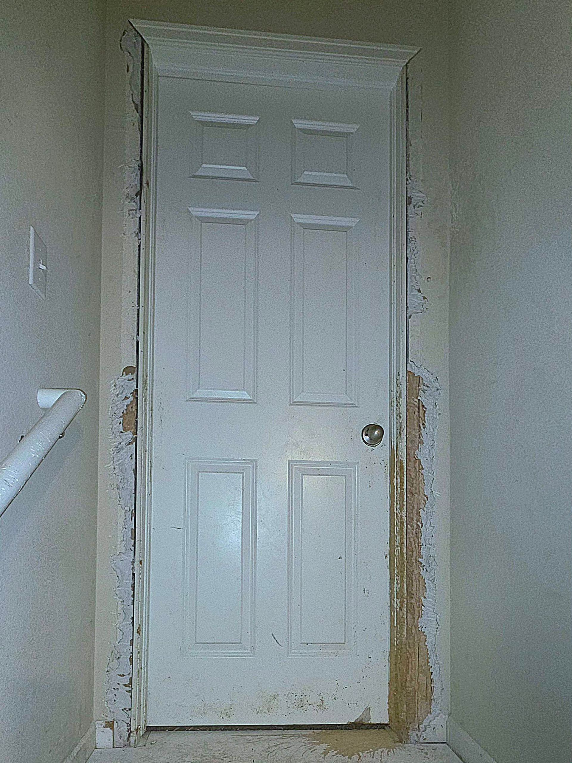 White door in a wall with damaged drywall and debris.