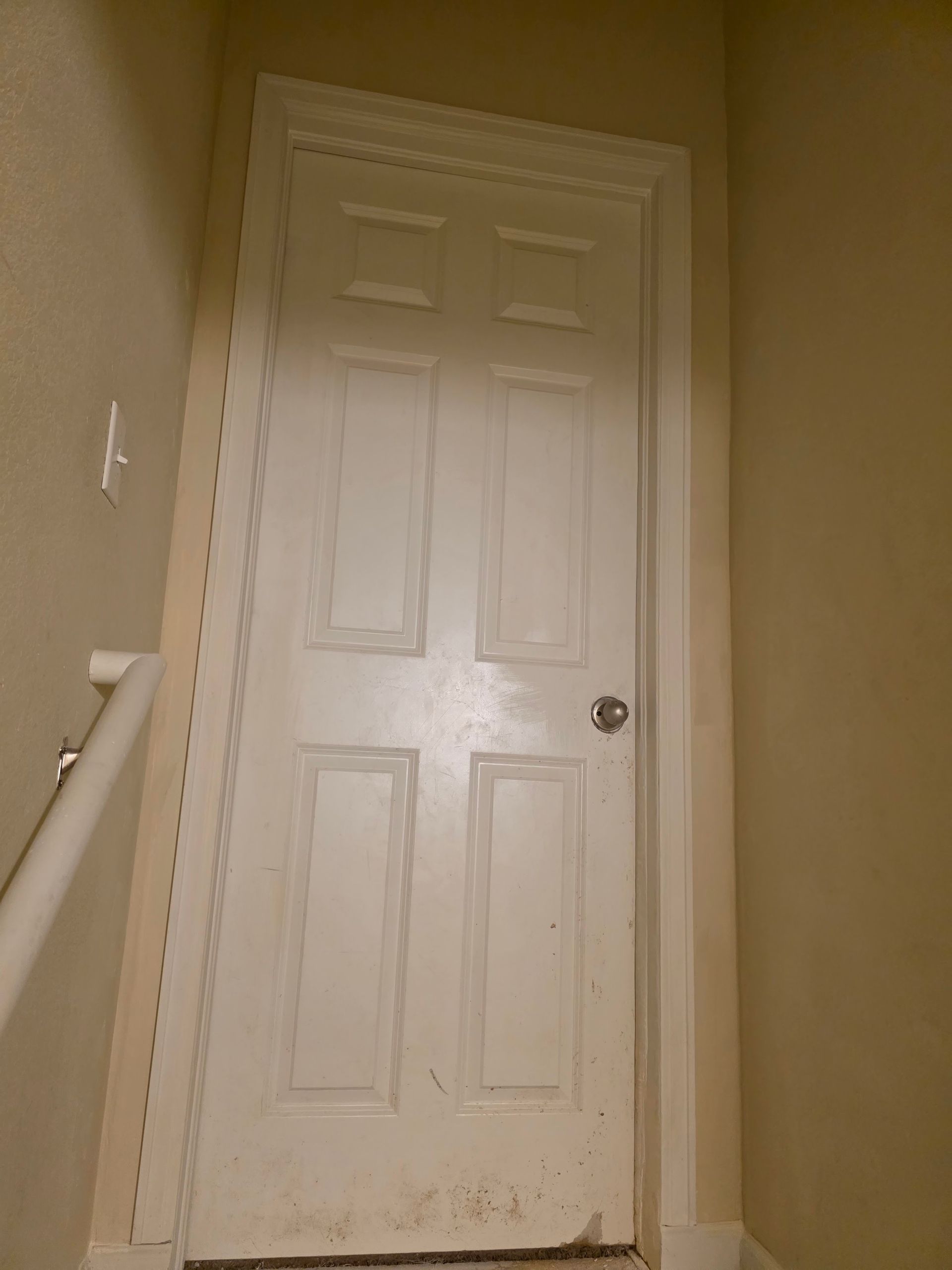 White door in a hallway at the top of stairs, with white trim and beige walls.