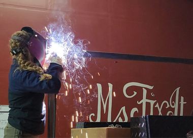 Welder in protective gear welding metal onto a red surface with 