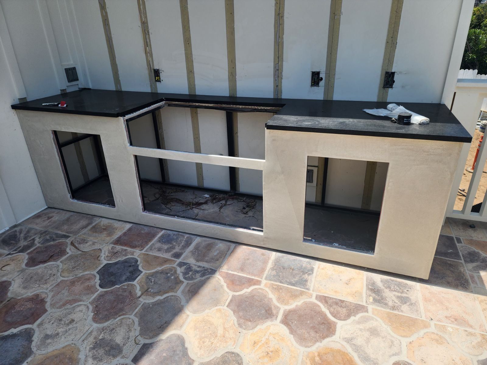 Outdoor built-in counter with black countertop, beige siding, and stone tile flooring.