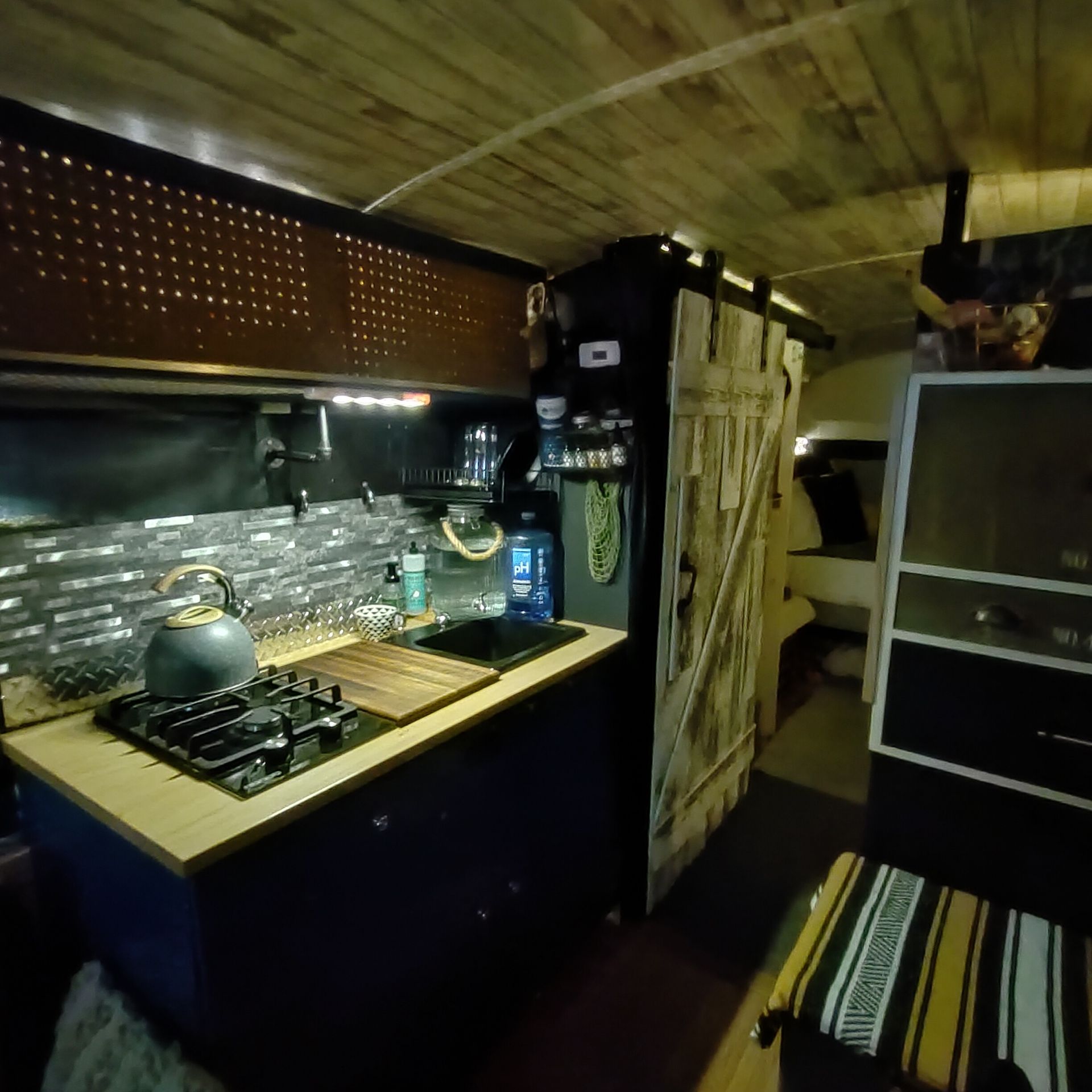 Cozy van interior with kitchen area: wood paneling, dark blue cabinets, sliding barn door.