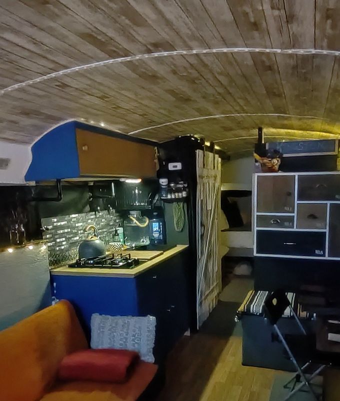 Interior of a renovated bus, featuring a kitchen area with blue and black cabinets, and a wood-paneled ceiling.