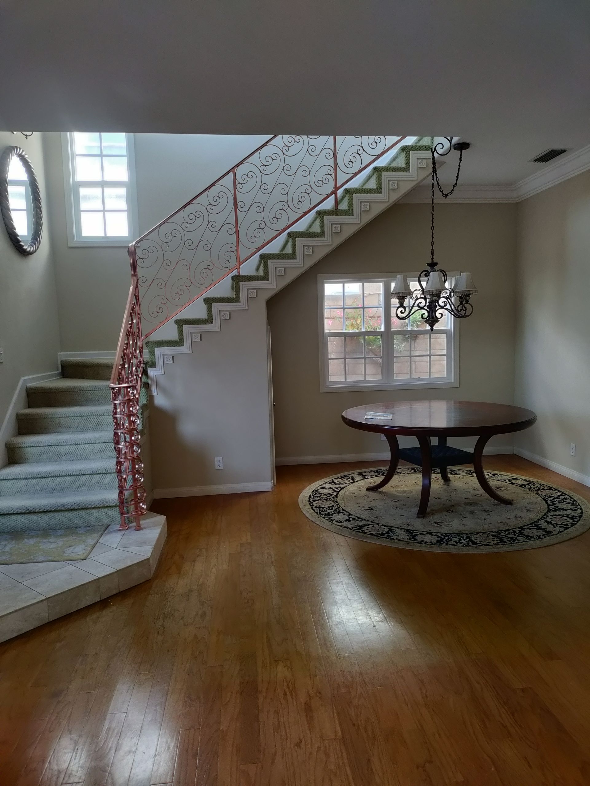 Staircase with floral-patterned railing next to a wood floor room, featuring a round table and chandelier.