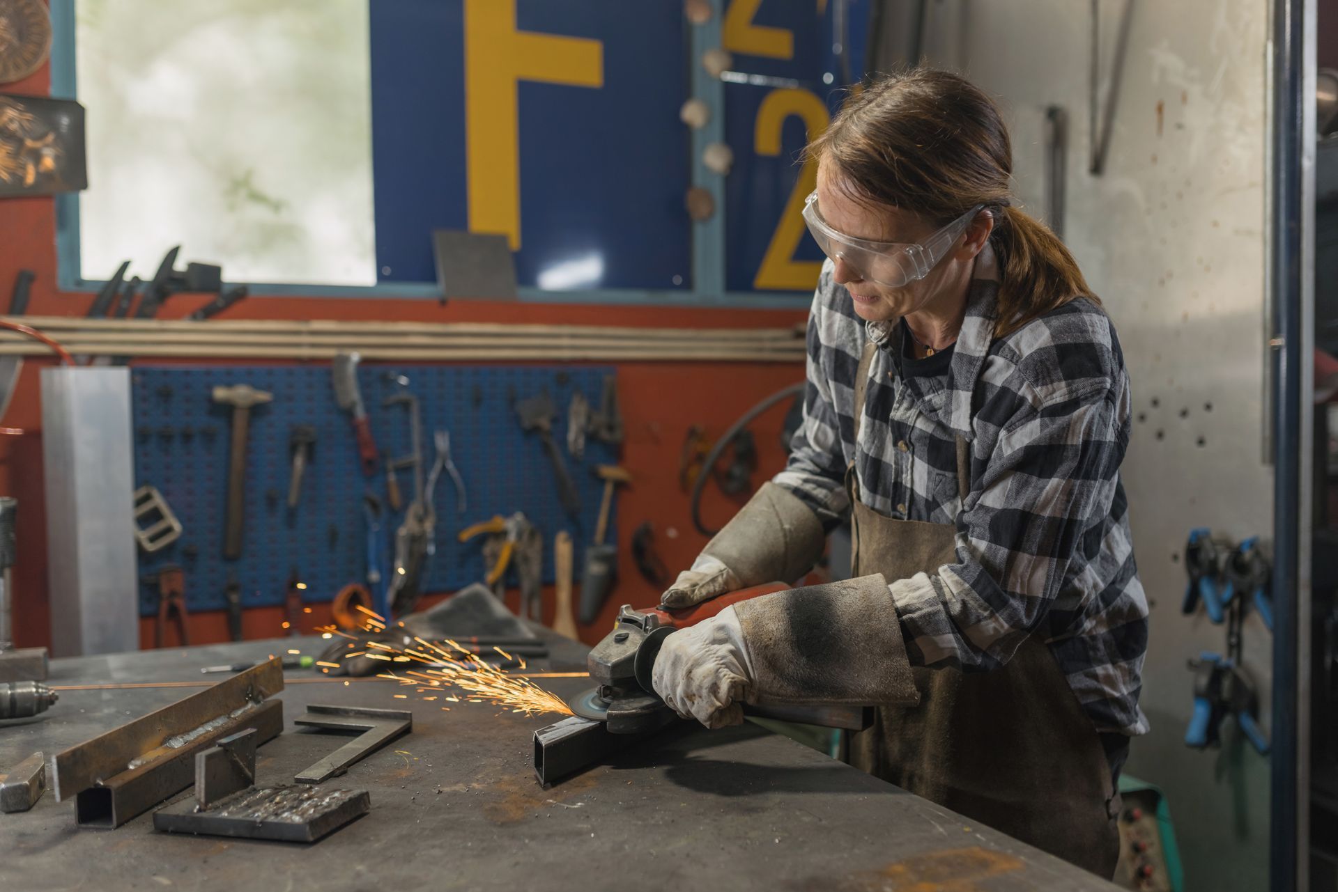 Woman wearing safety glasses grinds metal, sparks flying in workshop.