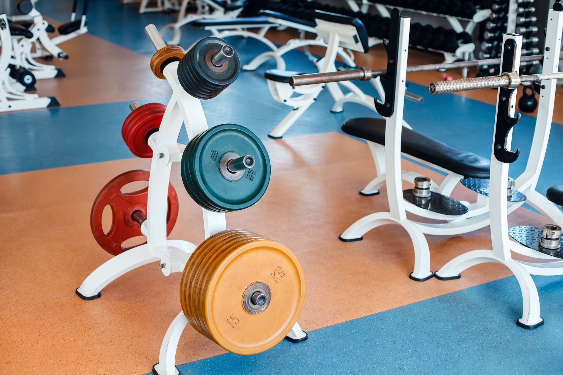 Weight plates on a stand, and a weight bench in a gym.