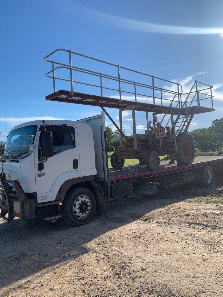 White Truck Carrying a Tractor With an Elevated Platform on a Dirt Road Under a Blue Sky — Quik As Couriers in Rosella, QLD