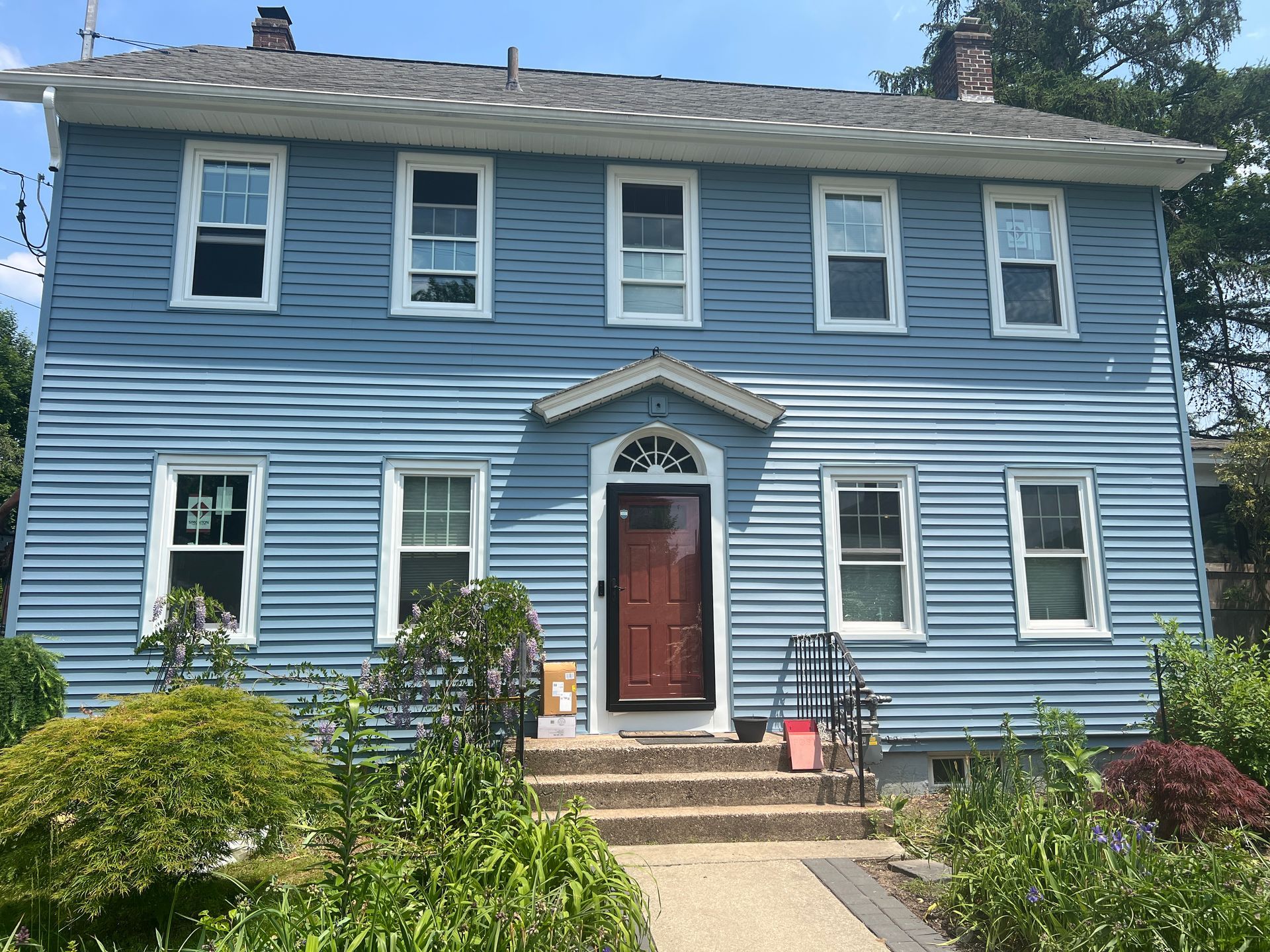 Blue two-story house with white trim and a brown door; sunny day.