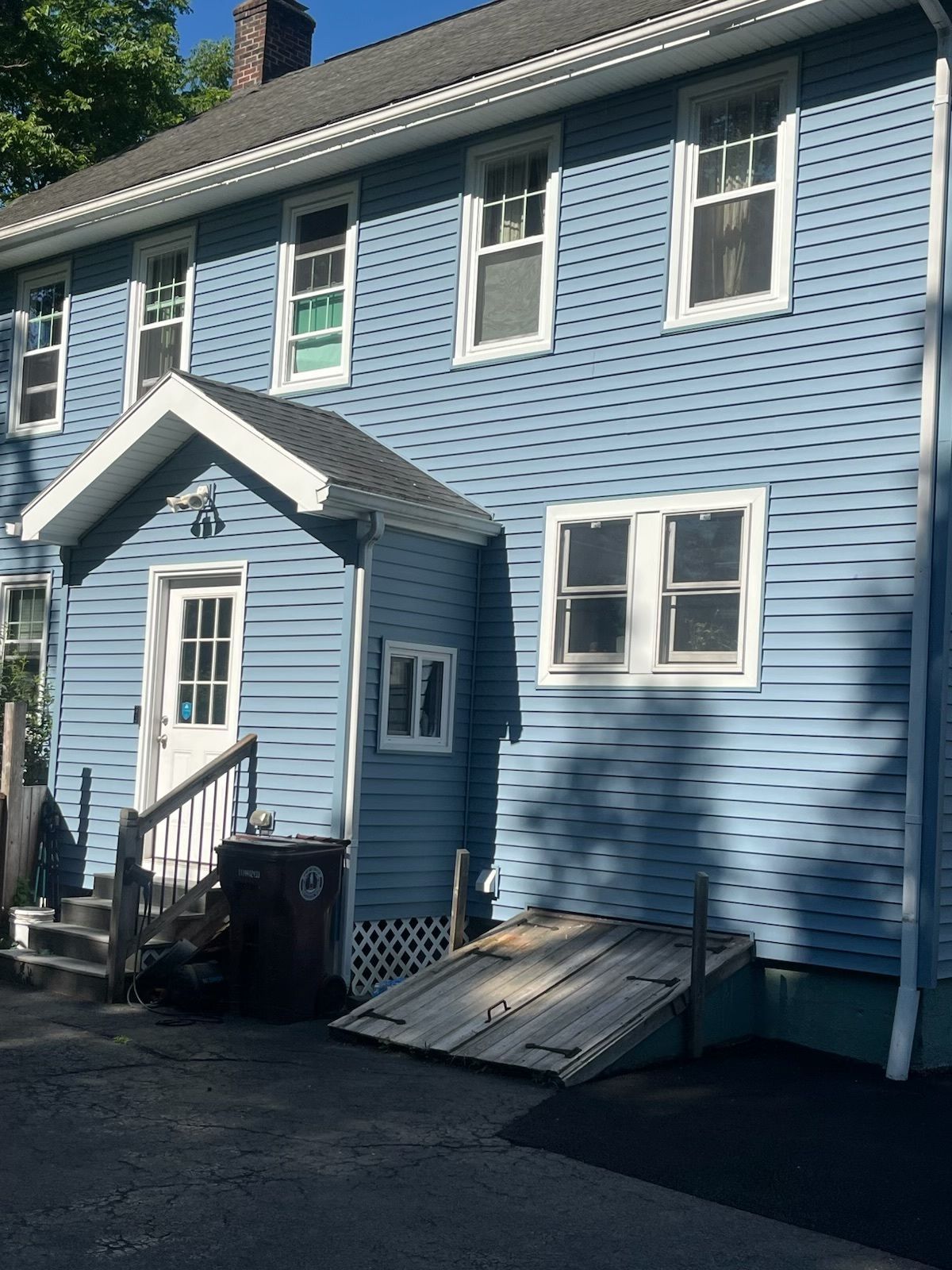 Blue two-story house with a small entrance porch, white trim, and a basement door.