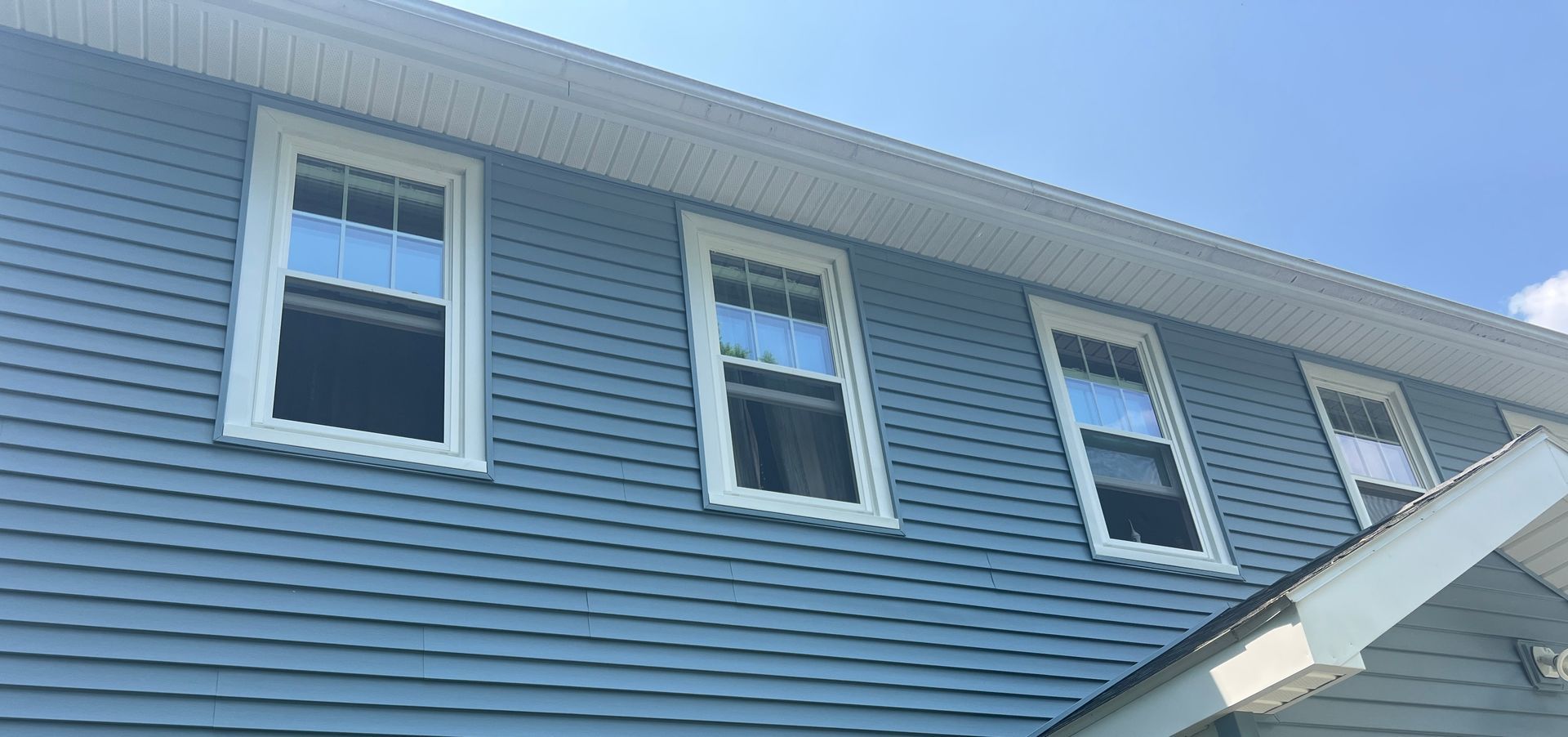 Blue-sided house with white window frames and trim against a clear, blue sky.