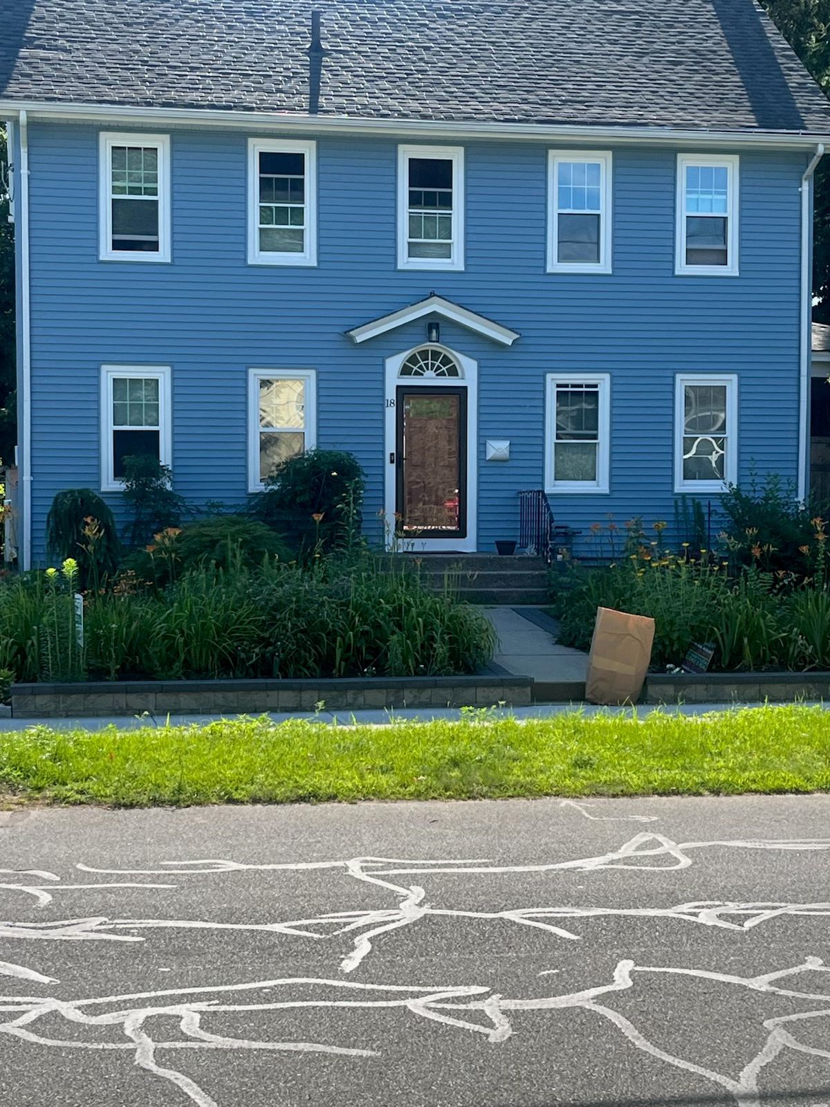 Blue two-story house with white trim, a door, and windows, with a garden in front.