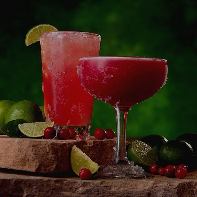 Due vivaci cocktail al mirtillo rosso, serviti in un bicchiere alto e in una coppa, guarniti con spicchi di lime e mirtilli rossi su una pietra.