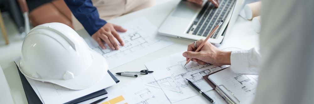 People Working On Blueprints And A Laptop, With A Hard Hat On The Table — GS Design & Drafting In Ballina, NSW