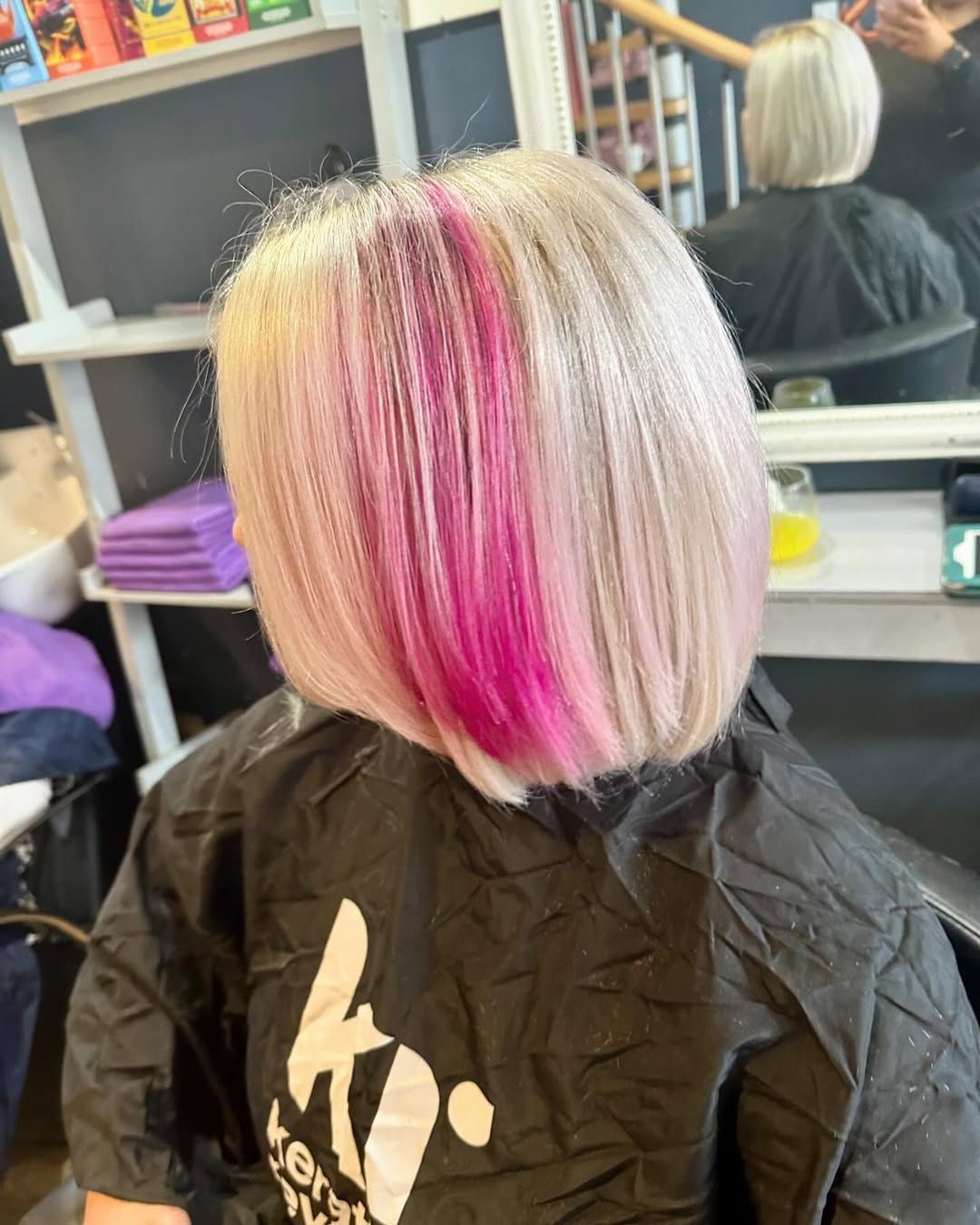 Short platinum bob with bright pink streaks in a salon chair, seen from behind