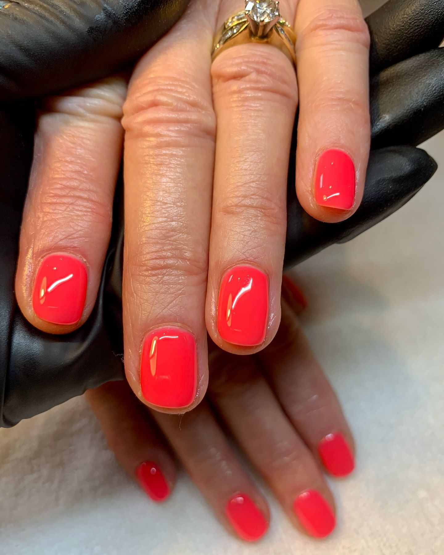 Close-up of hands with glossy neon pink manicured nails and gold ring