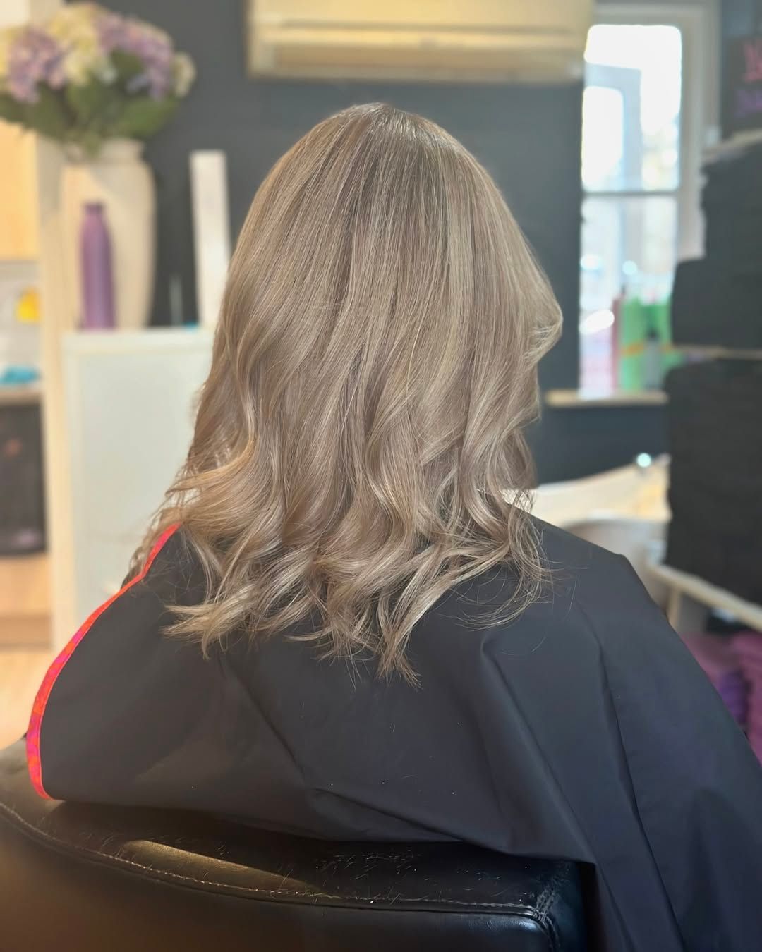 Person with shoulder-length gray hair seated in a salon chair, seen from behind.