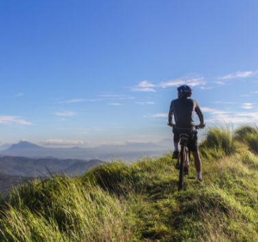 A person is riding a bike on top of a grassy hill.