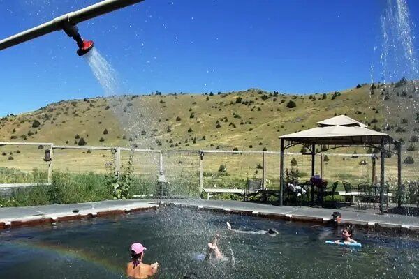 A group of people are swimming in a pool with a rainbow in the background.