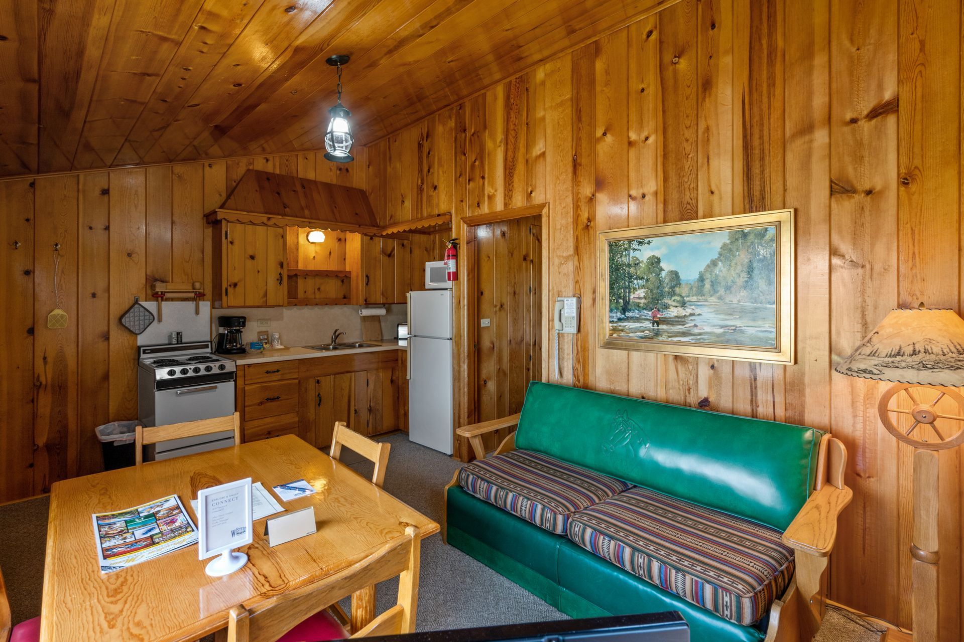 A living room with a green couch , table , chairs and a kitchen.