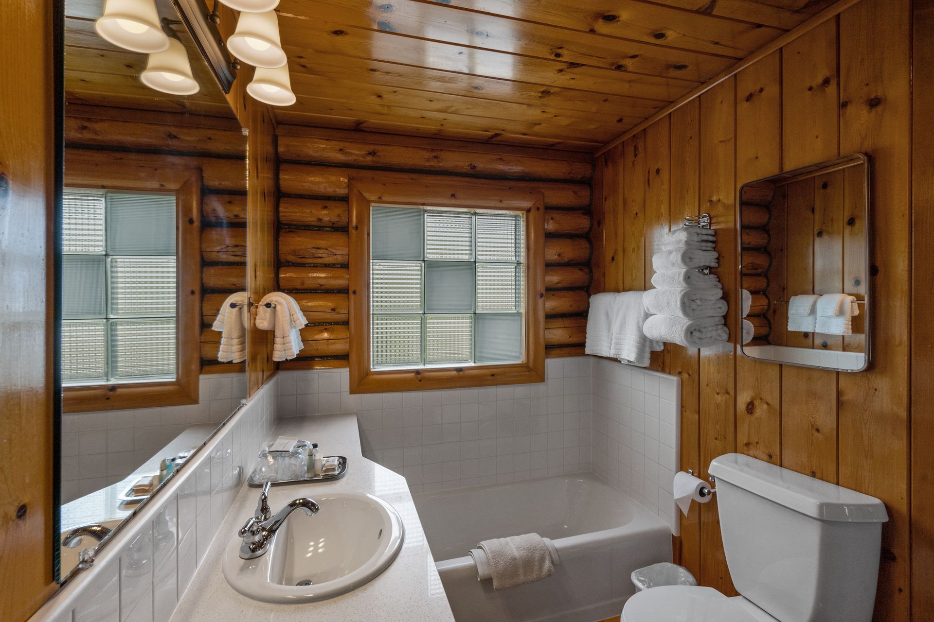 A bathroom in a log cabin with a toilet , sink , tub and mirror.