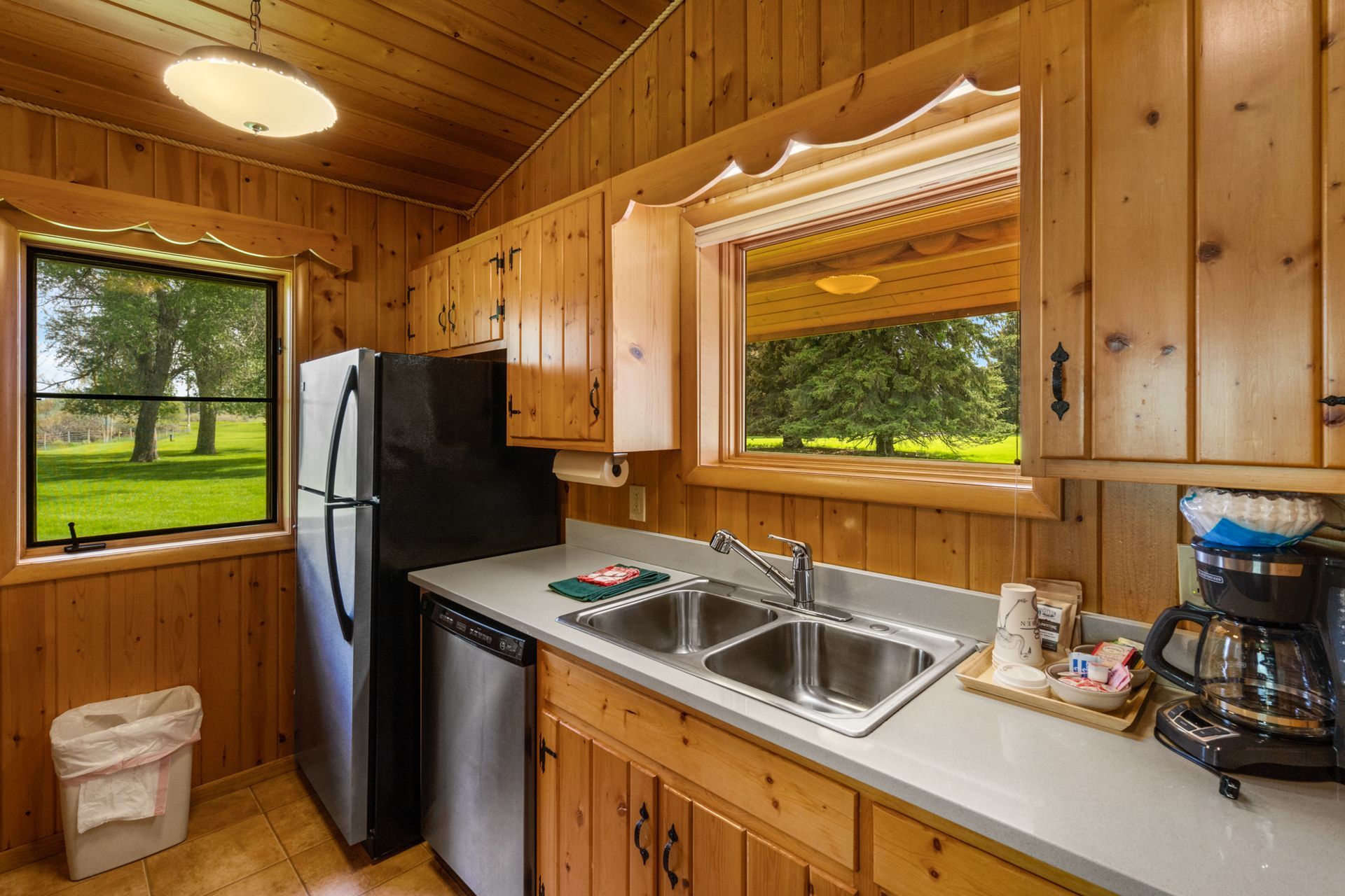 A kitchen with a refrigerator , sink , dishwasher , coffee maker and window.