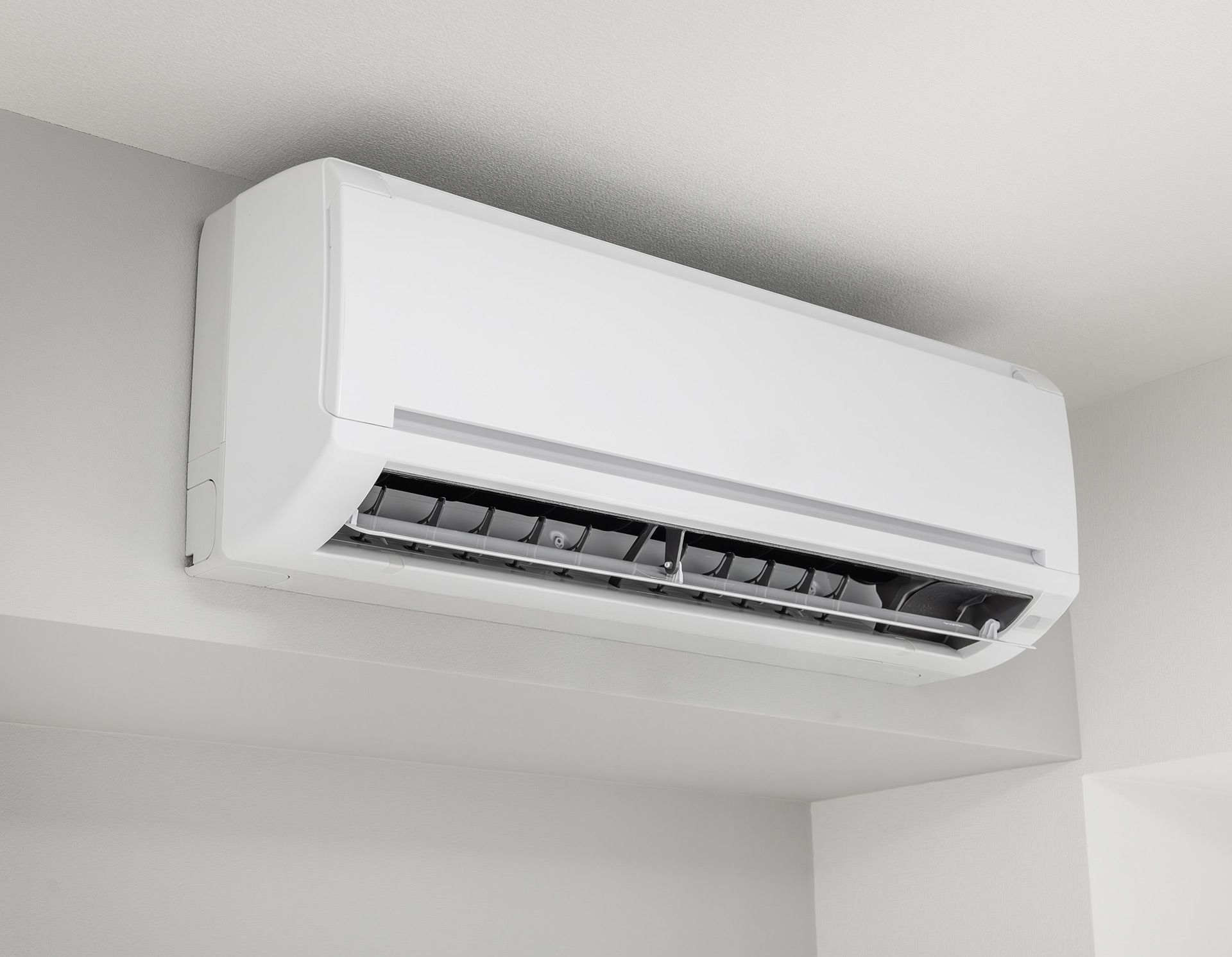 White wall-mounted air conditioner in a room corner, viewed from below.