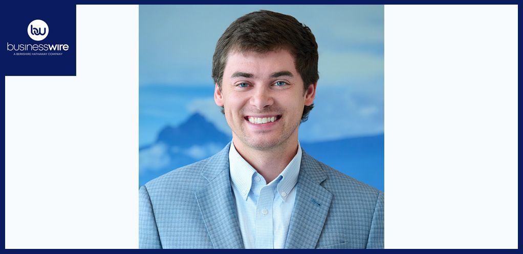 Dean Shahan wears a gray blazer and a light blue shirt, with a mountainous background.
