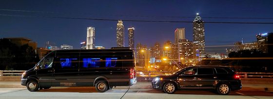 A van and a car are parked in front of a city skyline at night