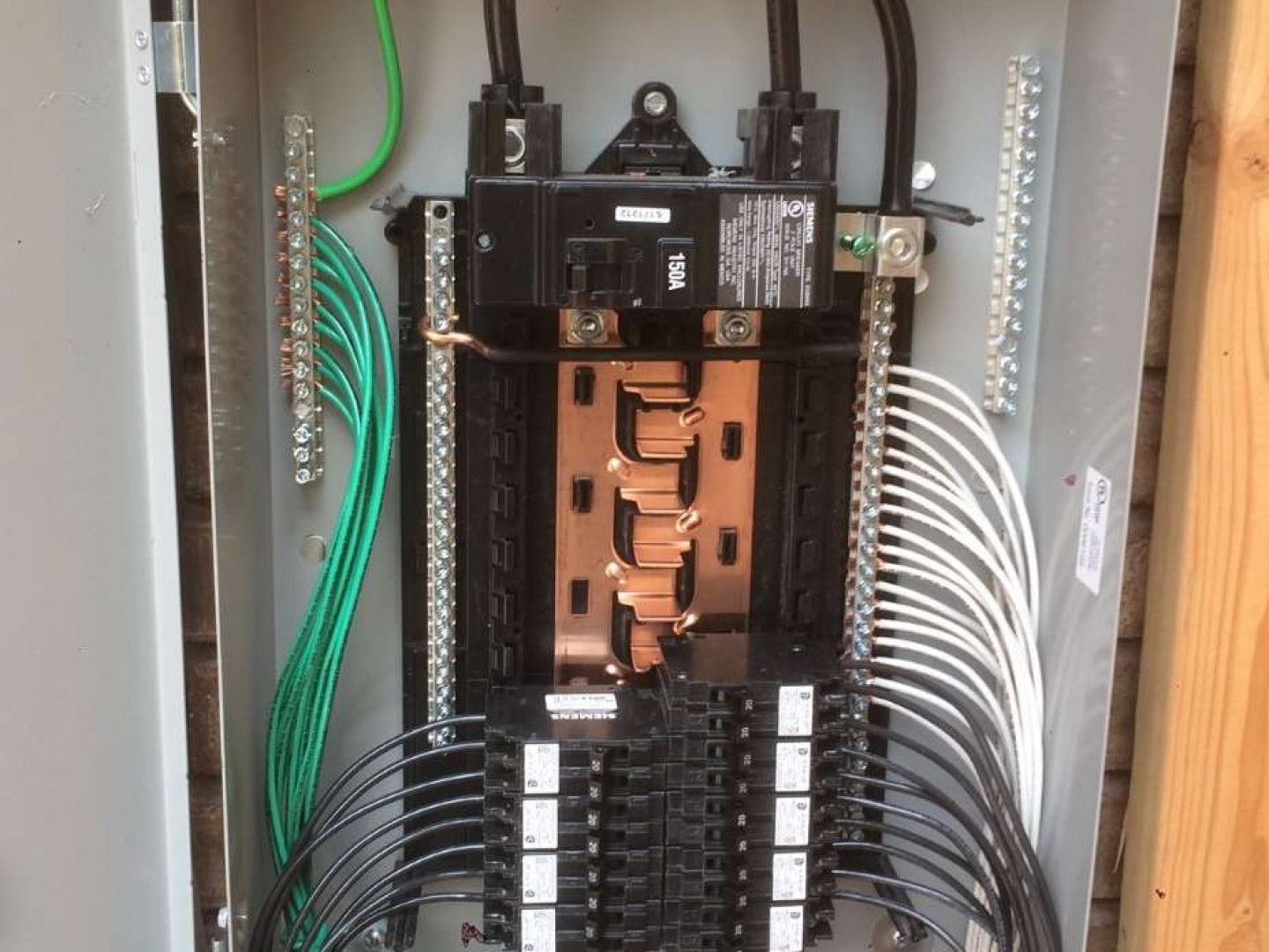 Open electrical breaker panel with wiring and labeled circuits inside a wall cavity