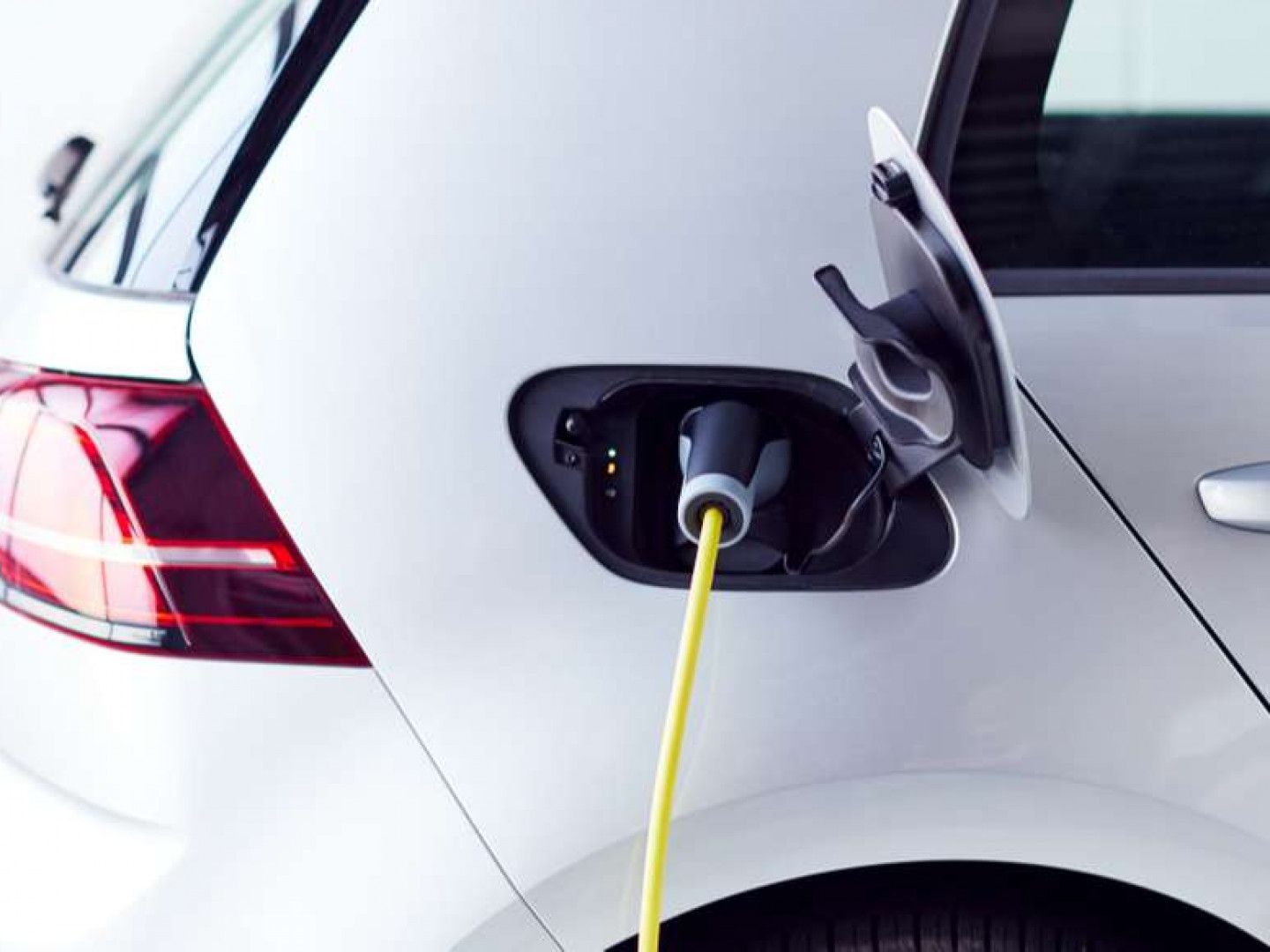 Electric car charging at a station, with a yellow cable plugged into the rear charging port.