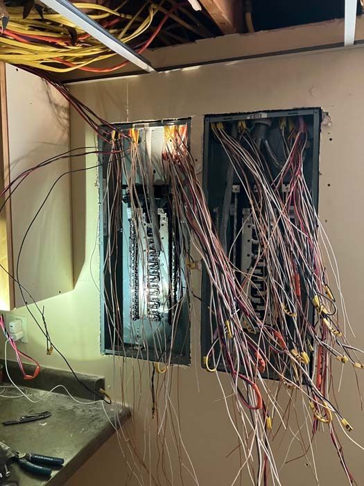 Messy electrical panel with tangled wires in a wall opening, viewed inside a room