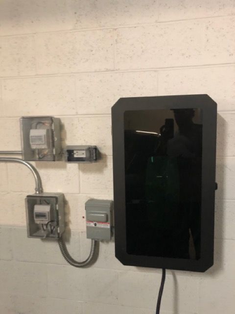 Wall-mounted electrical meters and a black framed screen on a white cinder block wall.