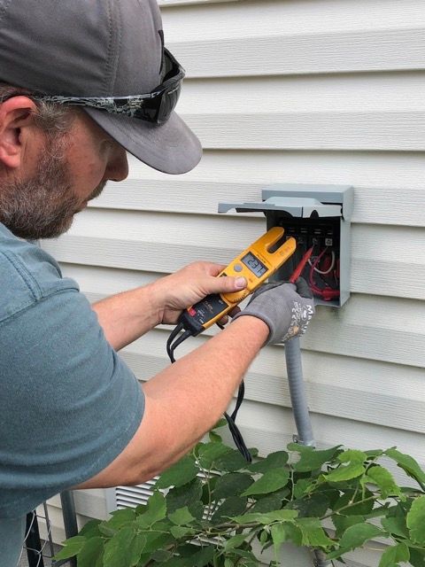 Technician testing outdoor electrical wiring at a house with a multimeter