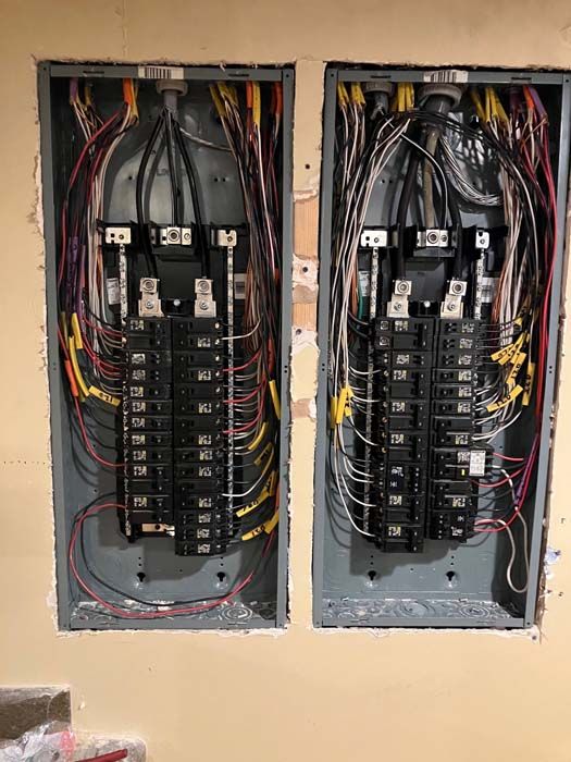 Two open electrical breaker panels with exposed wiring in a wall recess