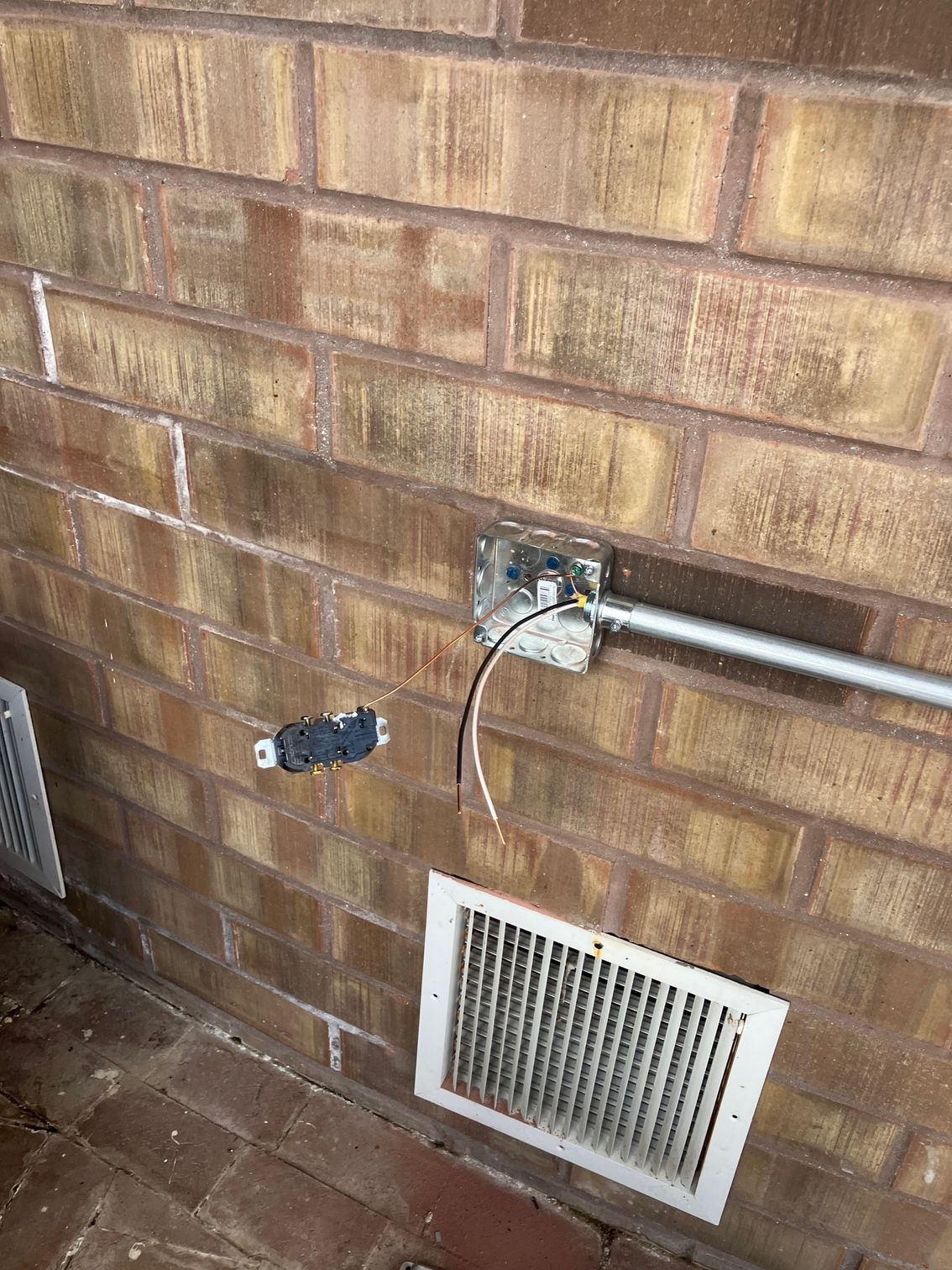 Brick wall with an electrical outlet, conduit, and a vent cover near the ground