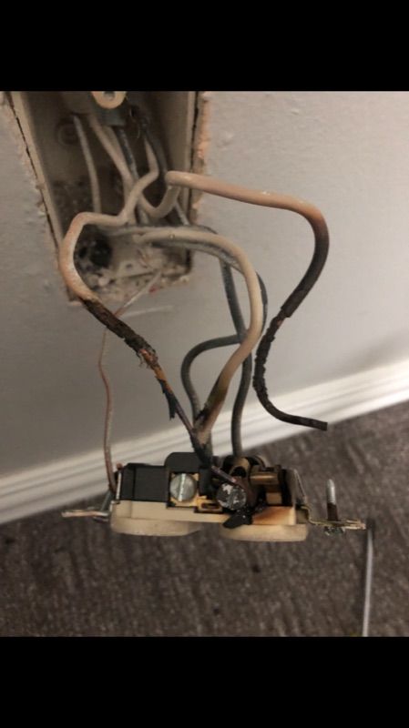 Exposed electrical outlet and loose wiring hanging from a wall above a carpeted floor.