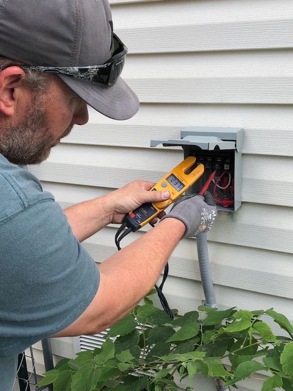 Technician testing outdoor electrical wiring with a voltage tester at a house wall