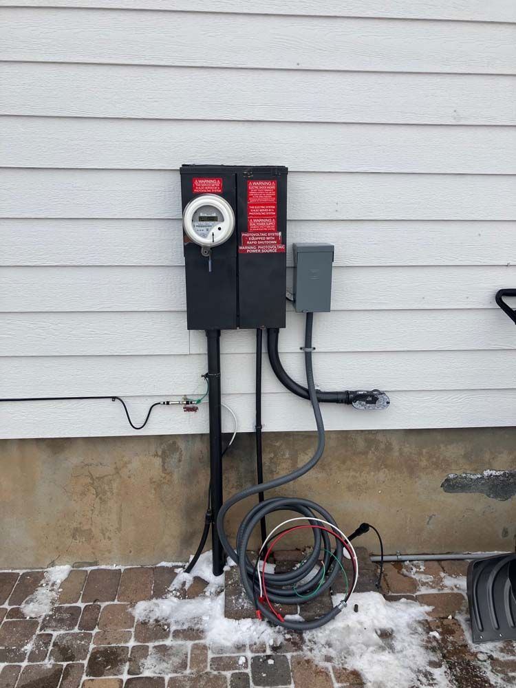 Electric utility meter and panel mounted on an exterior house wall with coiled cables below.
