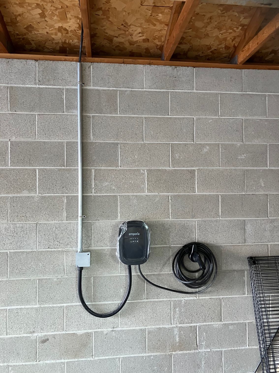 Utility box and conduit mounted on a cinder block wall under exposed wooden ceiling beams.