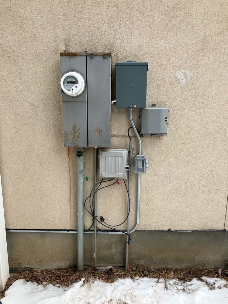 Utility meters and electrical boxes mounted on a beige exterior wall with some snow on the ground.