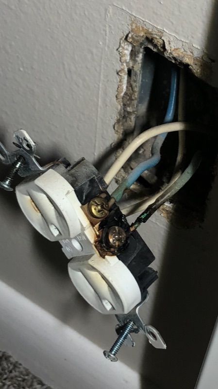 Damaged electrical outlet with exposed wires and scorch marks in a wall box