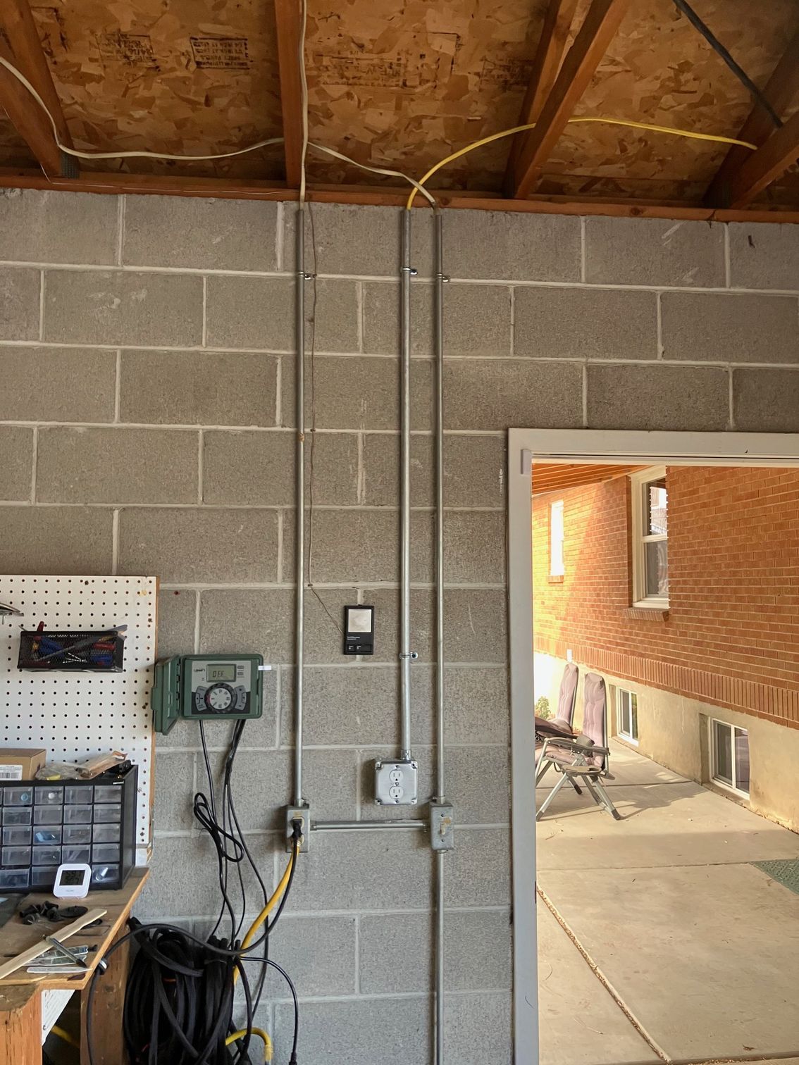 Workshop wall with cinder blocks, exposed ceiling beams, electrical boxes, and an open doorway to a brick walkway
