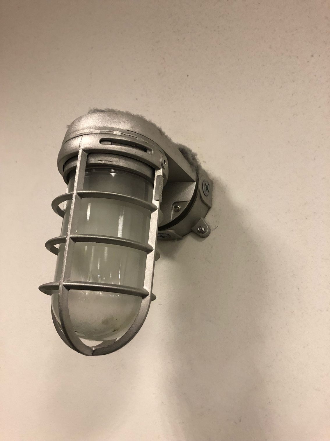 Wall-mounted metal cage light fixture with a frosted glass cover on a beige wall