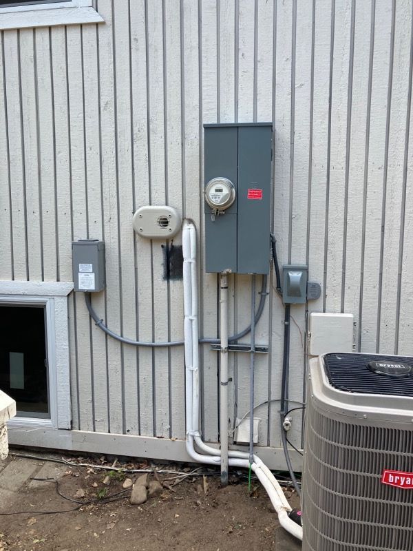 Exterior wall with electrical meter, utility boxes, and conduit beside an HVAC unit.