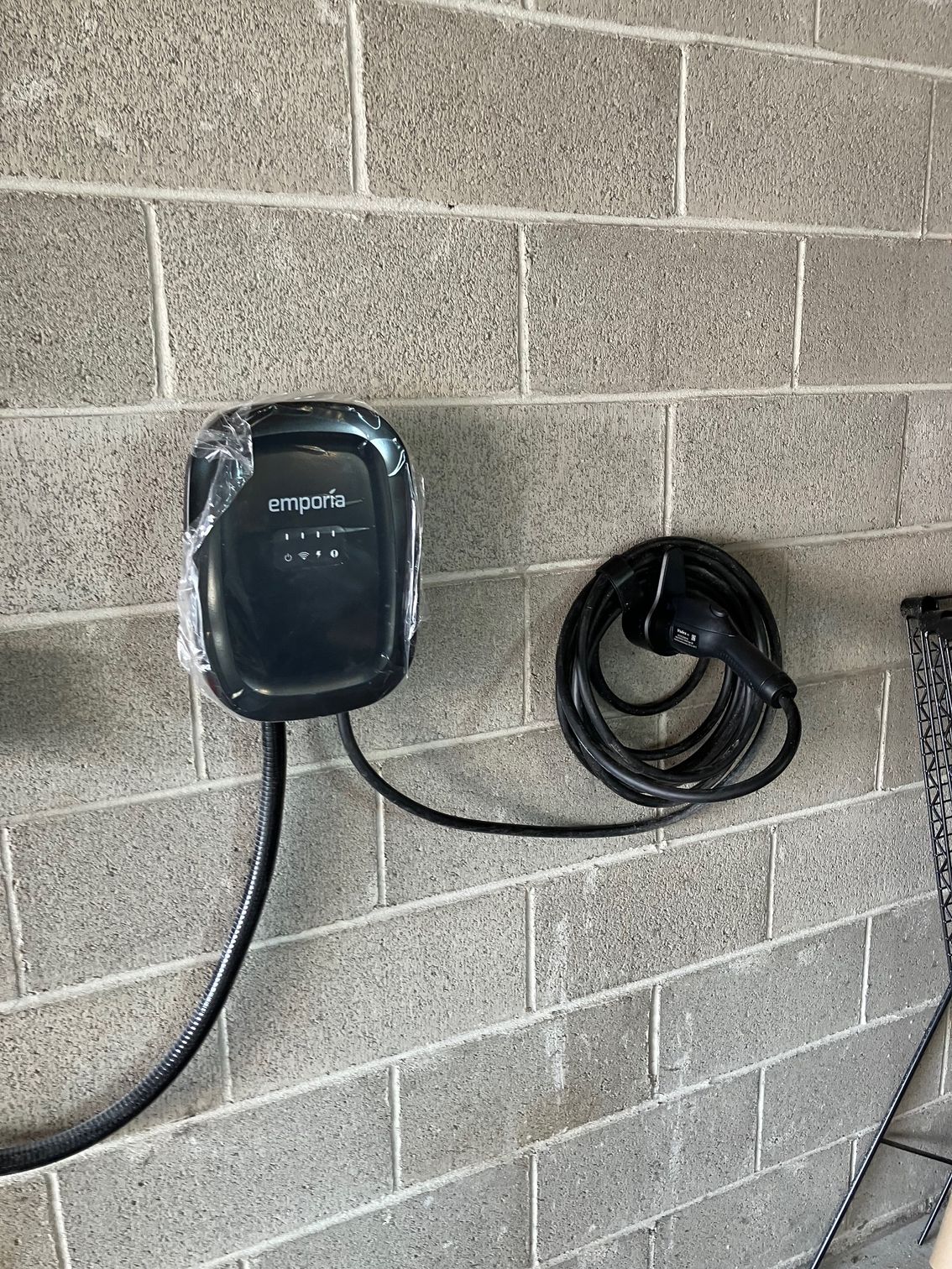 Black EV charger mounted on a cinder block wall with coiled charging cable.