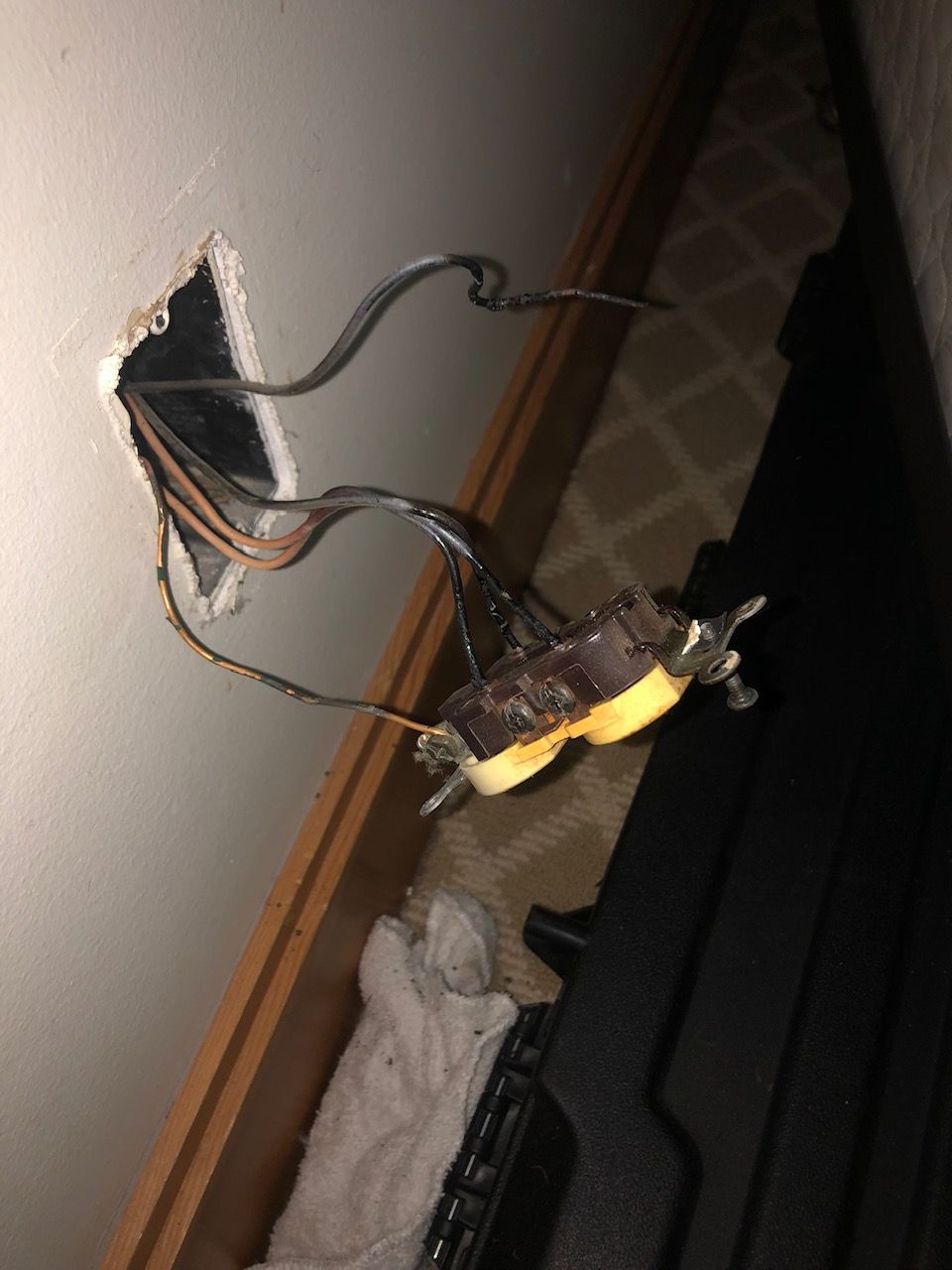 Broken wall switch with exposed wires hanging out of a wall opening.