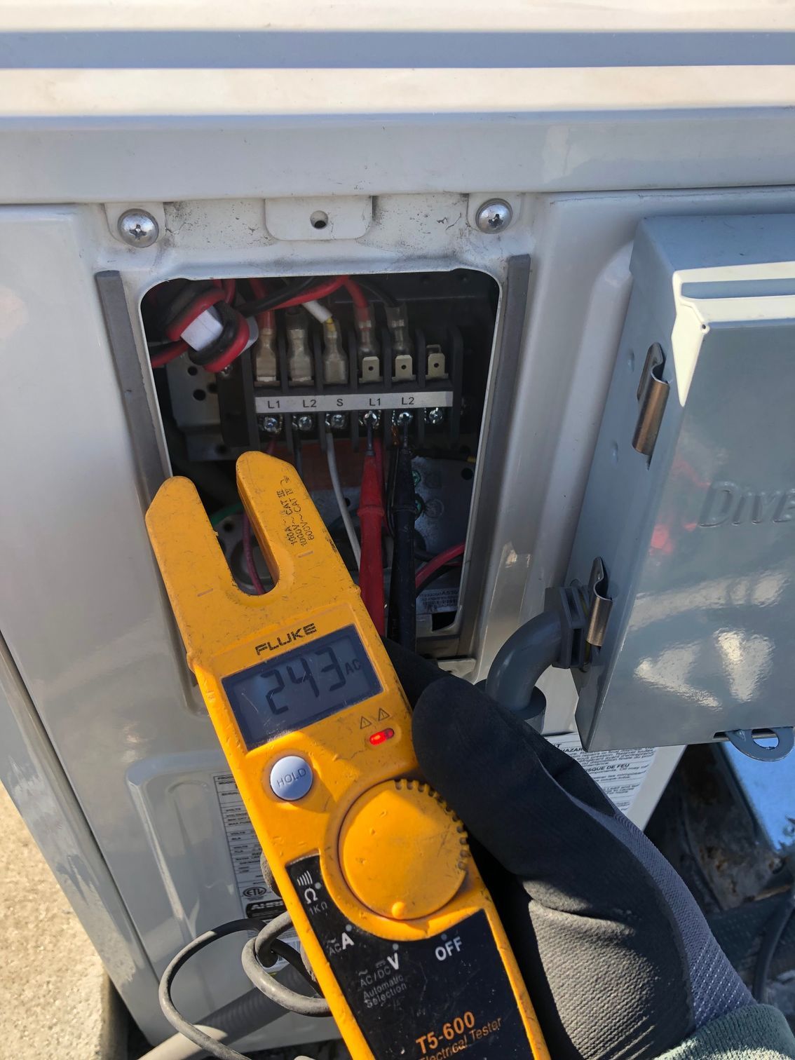 Gloved hand using yellow clamp meter to test electrical panel wiring with breaker switches open