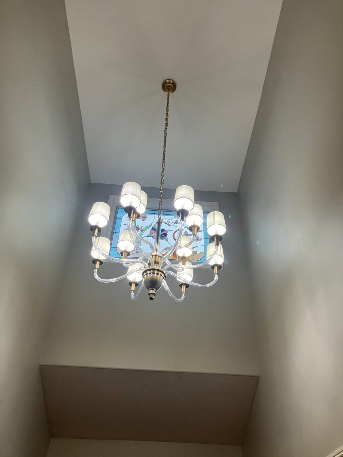 Chandelier hanging from a high ceiling in a stairwell, with white lamps and blue glass accents