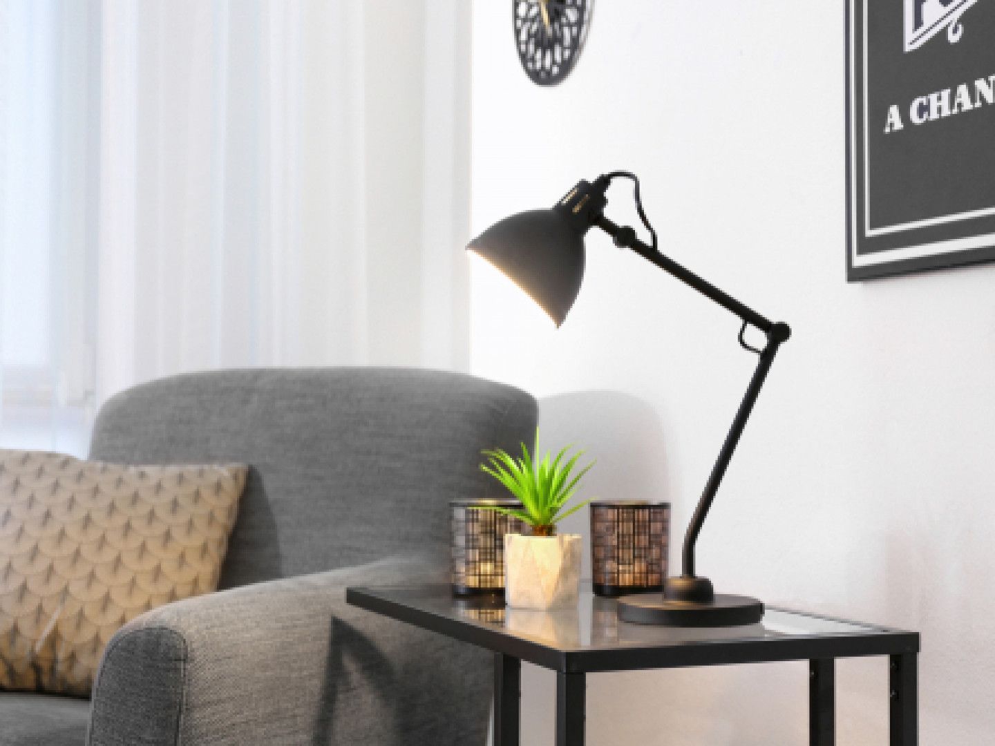 Gray armchair beside black side table with lamp and small plant in a bright living room.