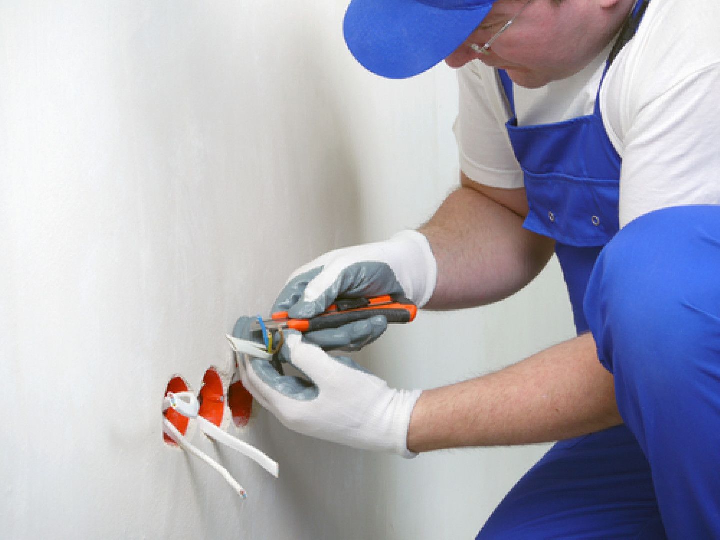 Technician in blue overalls using pliers to work on electrical outlets in a wall panel