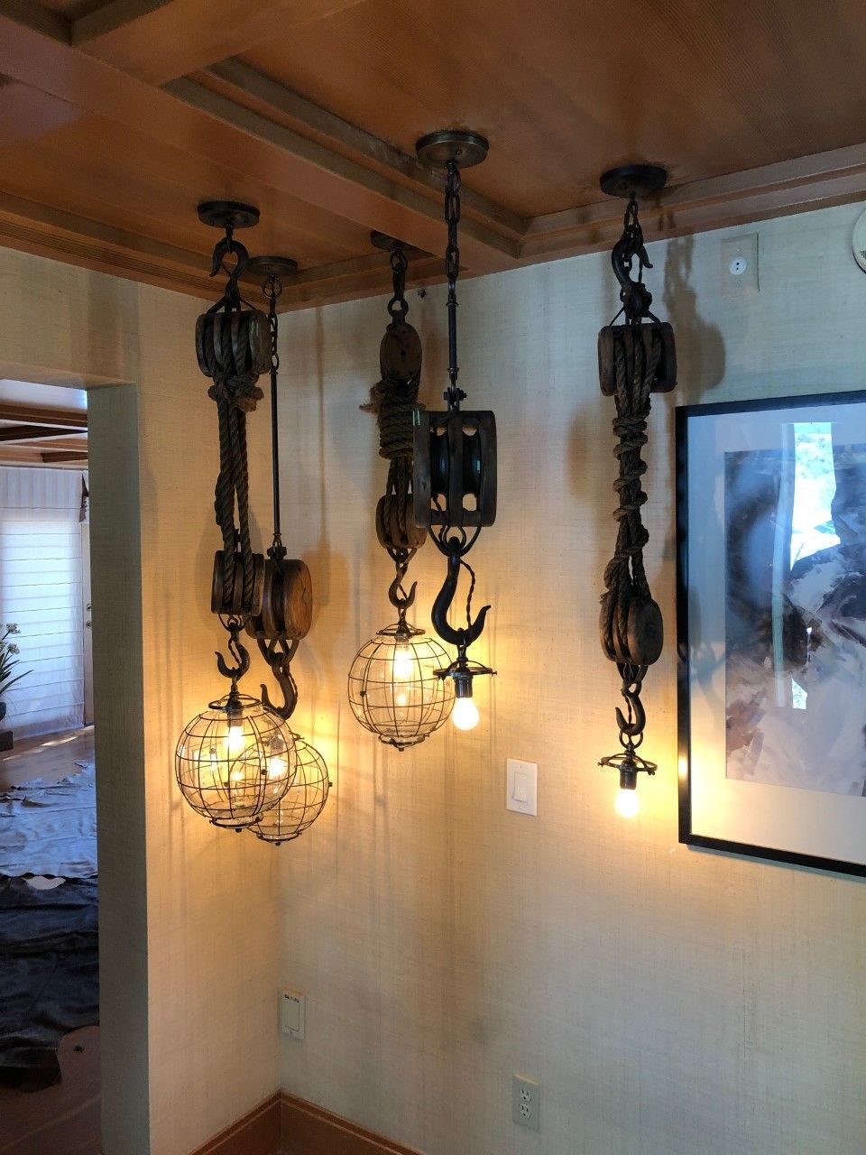 Three hanging vintage lanterns on a beige wall beside a framed artwork.